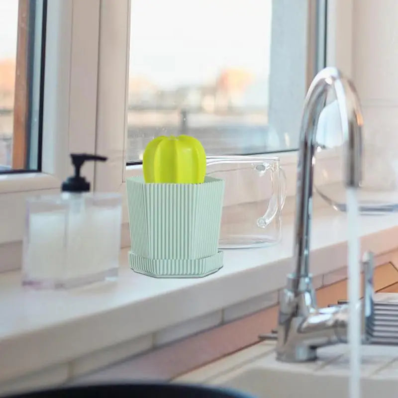 Dishwashing scrubber with cactus design in a sink, surrounded by cleaning supplies and a glass jug.